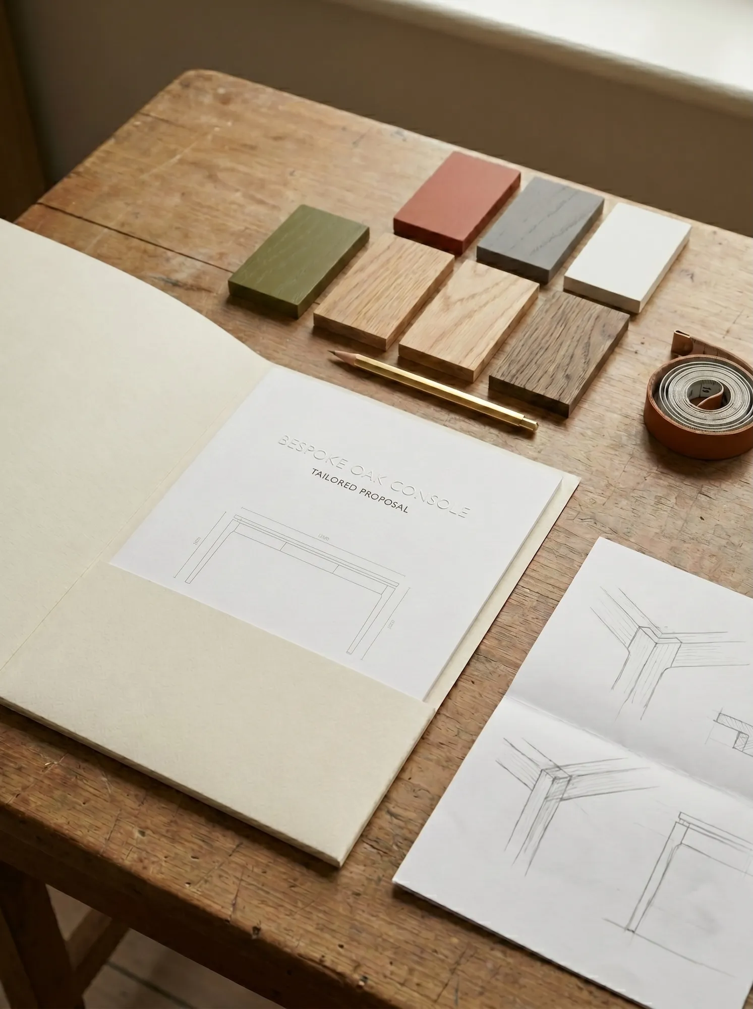Proposal document, oak finish sample, and handwritten dimensions on a warm studio table
